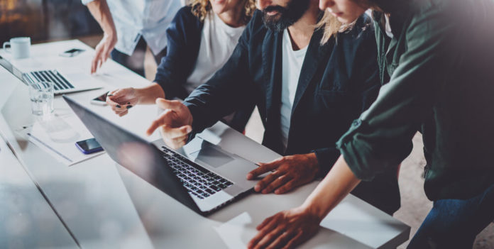 Working process at office. using laptops. Group of young coworkers work together modern coworking studio.Young people making conversation with partners.Horizontal Wide.Blurred background