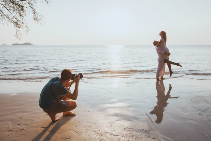 wedding and lifestyle photographer taking photos of affectionate couple on the beach at sunset