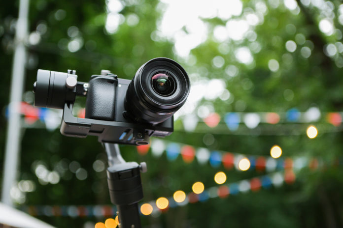 this is an image of A mirrorless camera with a stabilized monopod and remote control. On the background of the fair in the park