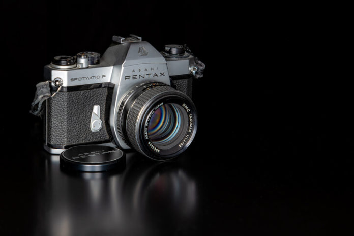 A Pentax film camera on a black table, with a black background.