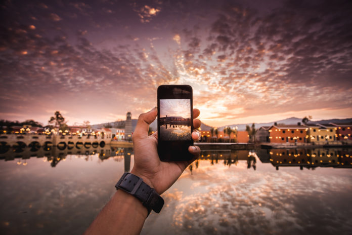 this is an image of a hand taking a photo a sunset on an iPhone