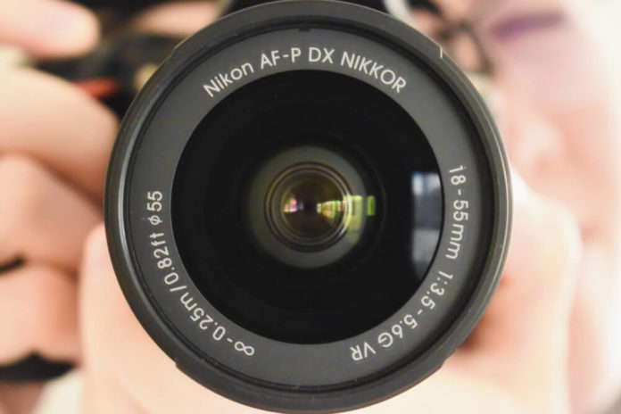Closeup picture of the camera lens of the Nikon d5600 dslr, held by a photographer.